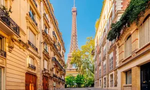 Vue sur la Tour Eiffel entre deux immeubles parisiens, un jour férié de mai. Les balcons ornés et les façades en pierre rappellent le charme de la capitale.