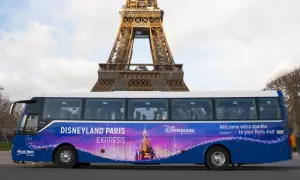 Un bus Disneyland Paris Express, décoré d'un château féerique, passe devant la Tour Eiffel.