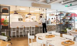 Un restaurant italien moderne avec un four à pizza visible. Des chefs préparent des plats derrière le comptoir, tandis que des tables sont dressées pour les clients.