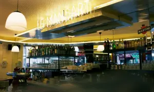 Bar lumineux avec enseigne néon "LE MANSART PARIS". Bouteilles d'alcool et verres alignés sur les étagères.