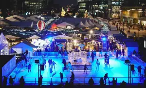 Patinage sur glace et marchés de Noël ouverts, illuminés par des lumières bleues vives. Une scène festive avec des chalets et des décorations scintillantes.