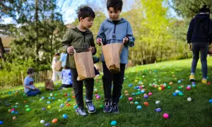 Deux enfants cherchent des œufs colorés dans l'herbe lors d'une chasse aux œufs à Paris.