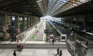 Intérieur lumineux de la gare du Nord, avec des quais, des voies ferrées et des trains. Des voyageurs circulent sous la grande verrière.