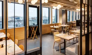 Restaurant moderne avec vue sur Paris. Tables dressées, lumières douces, et le logo "Printemps du Goût" visible.