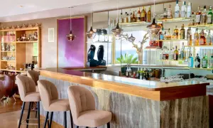 Un **majestic bar** avec des tabourets beiges, des étagères remplies de bouteilles et une vue sur la mer.
