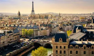 Vue panoramique de Paris en mars, avec la Tour Eiffel dominant un ciel clair. Les toits gris et les bâtiments haussmanniens s'étendent à perte de vue.