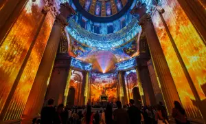 Spectacle lumineux projeté sur des colonnes et un dôme, créant une aura de couleurs vives. Une foule admire cette installation, comme si les dates invalides s'effaçaient.