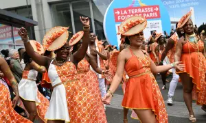 Des danseuses en tenues orange et blanches, chapeaux assortis, célèbrent la foire de Paris 2026 dans une ambiance festive.