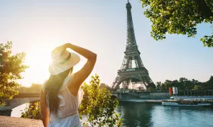 Une femme au chapeau admire la Tour Eiffel au coucher du soleil, profitant des activités parisiennes.