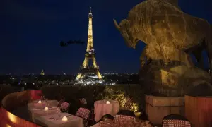 Vue nocturne de Paris avec la Tour Eiffel illuminée. Un bar ouvert le 25 décembre, avec des tables dressées et une statue de taureau. Le traîneau du Père Noël traverse le ciel.