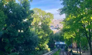 Vue sur le funiculaire de Montmartre, avec Paris en arrière-plan. Les arbres verdoyants encadrent la scène.