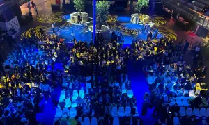 Vue aérienne d'une foule assise dans une **arena Paris** illuminée de bleu, avec des motifs jaunes au sol.