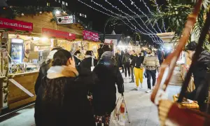 Ambiance féerique d'un marché de Noël à Paris. Des chalets en bois illuminés proposent des spécialités, tandis que des passants flânent sous les guirlandes lumineuses.