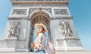 Une jeune femme tend la main devant l'Arc de Triomphe. L'accès au monument est gratuit, une belle opportunité de visite.