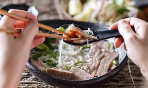 Une cuillère de ce meilleur pho, remplie de nouilles, de viande et d'une touche de sauce piquante, est soulevée avec des baguettes.