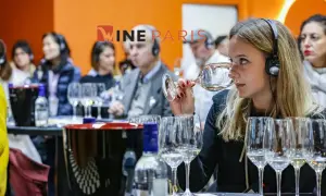 Dégustation de vin à Wine Paris 2026. Une femme hume un verre, casque sur les oreilles, entourée d'autres participants.