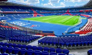 Vue panoramique du **Parc des Princes** vide, avec ses tribunes bleues et rouges, son terrain de football verdoyant et le logo du PSG au centre.