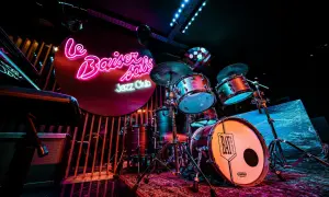 Batterie de jazz dans un bar parisien, éclairé par des néons roses et bleus. Ambiance feutrée pour une soirée musicale.