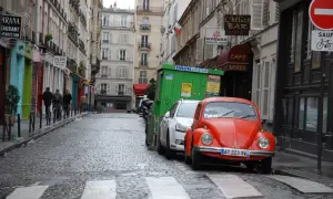 Une rue pavée à Paris, avec une Coccinelle rouge garée. Un panneau "parking gratuit Paris" serait le bienvenu ici.