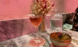 Un cocktail rose et un bol de fruits sur un marbre rose, ambiance douce et romantique d'un bisou bar.