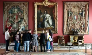 Visiteurs admirant le portrait de Louis XIV et des tapisseries grandioses, une scène digne des 50 plus beaux tableaux du Louvre.