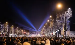Une foule nombreuse célèbre une **soirée paris** sous les lumières bleues illuminant l'Arc de Triomphe et les arbres décorés de guirlandes.