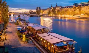 Un restaurant sur Seine à Paris, illuminé et accueillant, reflète ses lumières sur l'eau paisible.