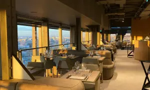 Intérieur d'une brasserie chic avec vue panoramique sur Paris. Les tables sont dressées, prêtes à accueillir les clients pour un dîner inoubliable à la Madame Brasserie Tour Eiffel.