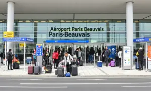 Voyageurs avec bagages devant l'aéroport Paris-Beauvais, prêts pour leur vol.