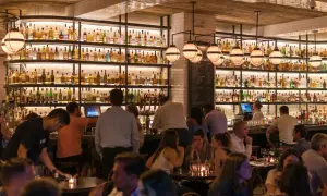 Ambiance chaleureuse dans ce bar gay, avec des étagères remplies de bouteilles et des clients attablés.