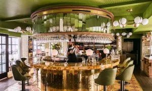 Barman préparant un cocktail dans un bar chic aux murs verts et au comptoir doré. Une ambiance de "pink mama" pour une soirée réussie.