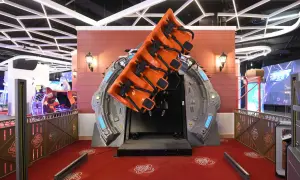 Attraction de manège orange suspendue, prête à faire décoller les visiteurs. Le sol rouge est décoré de motifs "La tête dans les nuages".