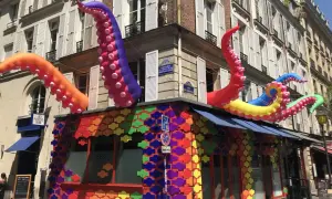 Tentacules colorés géants sortent d'un bâtiment orné de motifs arc-en-ciel, un décor festif pour ce bar gay à Paris.