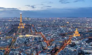 Vue panoramique de Paris au crépuscule, avec la Tour Eiffel illuminée et le dôme des Invalides. On aperçoit le quartier de La Défense au loin. Un panorama depuis l'**étage tour Montparnasse**.