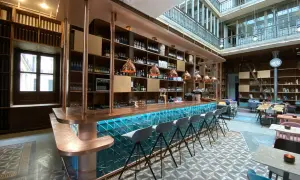 Le bar moderne du "Le Shack Paris" avec son comptoir en cuivre et ses tabourets gris, baigné de lumière naturelle.