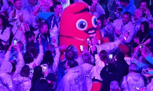 La Phryge JO, mascotte des JO, interagit avec une foule joyeuse. Les gens filment et prennent des photos avec leurs téléphones.