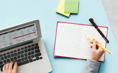 Planification des jours fériés 2026 sur un calendrier d'ordinateur. Une main écrit dans un carnet à côté.