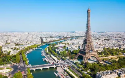 Vue aérienne de Paris avec la tour Eiffel dominant la ville. La Seine serpente à travers le paysage urbain, bordée d'arbres et de ponts.