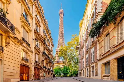 Vue sur la Tour Eiffel entre deux immeubles parisiens, un jour férié de mai. Les balcons ornés et les façades en pierre rappellent le charme de la capitale.