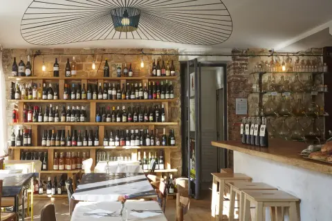 Ambiance chaleureuse dans la cave à manger, avec des étagères remplies de bouteilles de vin, des tables dressées et un bar en bois.