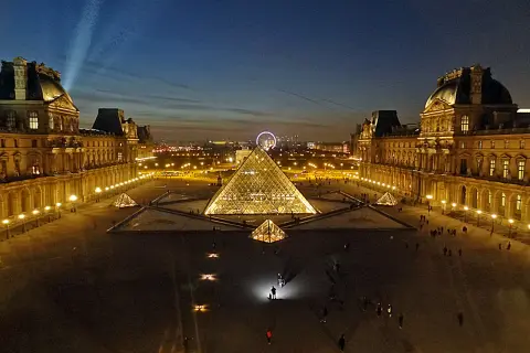 La Pyramide du Louvre illuminée, une belle soirée du 14 juillet. La foule admire le spectacle nocturne.