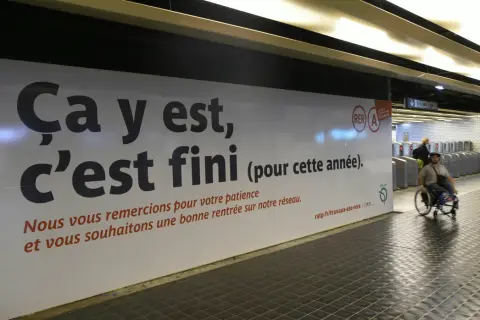 Panneau RATP annonçant la fin des travaux sur le RER A. Une personne en fauteuil roulant passe devant.