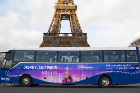 Un bus Disneyland Paris Express, décoré d'un château féerique, passe devant la Tour Eiffel.