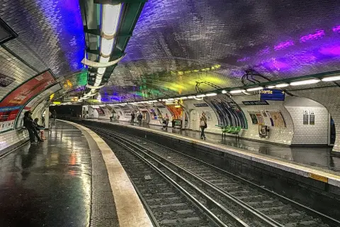 Le quai du métro Arts et Métiers, illuminé par des lumières colorées rappelant un atelier des lumières, attend les voyageurs.