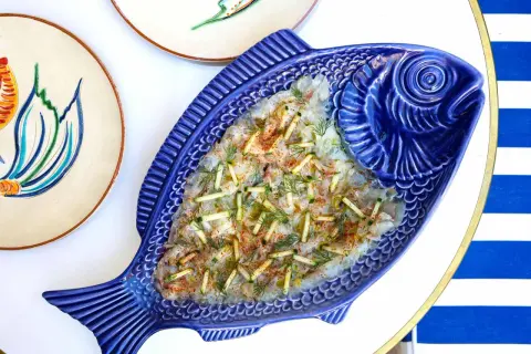 Un délicieux carpaccio de poisson servi dans un plat bleu en forme de poisson, parfait pour un déjeuner à Paris.