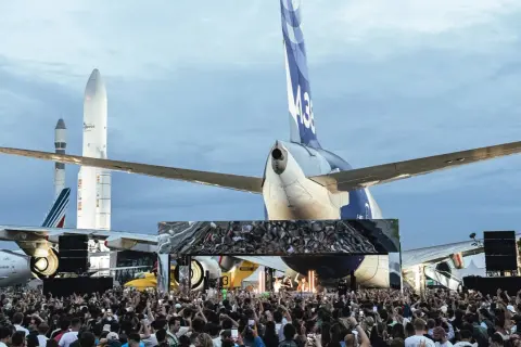 Foule immense devant une scène, sous des avions et des fusées. Ambiance de festival Cercle.