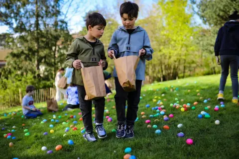 Deux enfants cherchent des œufs colorés dans l'herbe lors d'une chasse aux œufs à Paris.