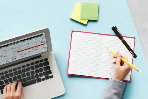 Planification des jours fériés 2026 sur un calendrier d'ordinateur. Une main écrit dans un carnet à côté.