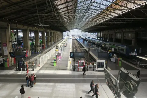 Intérieur lumineux de la gare du Nord, avec des quais, des voies ferrées et des trains. Des voyageurs circulent sous la grande verrière.