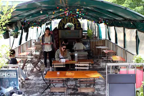 Terrasse animée d'un café-restaurant sur une péniche à Paris, avec des tables en bois, des lumières colorées et des plantes.